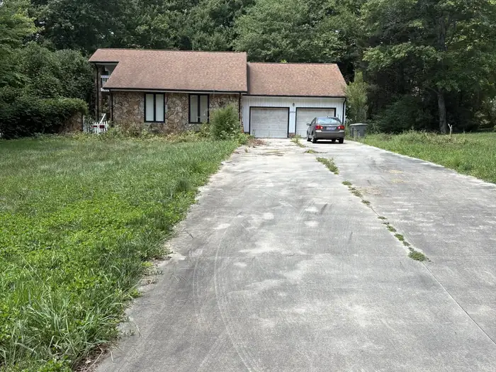A long driveway before, with weeds in the cracks and tall grass beside it