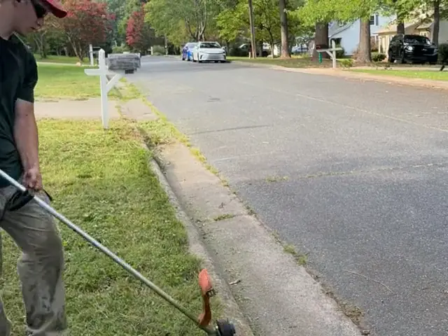 Edging along a curb with a string trimmer, dust flying off the concrete